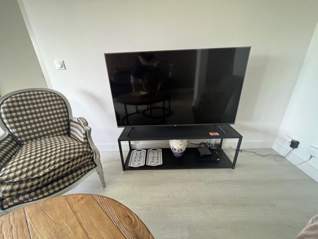 A living room with a large flat-screen TV on a black stand, a patterned armchair, and a wooden coffee table.