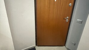 A wooden door with a handle and a lock, a black doormat, and a light switch on the wall. - Pretty Studio Flat Moglio Alassio (Moglio)