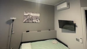 A bedroom with a bed, a ceiling light fixture, an air conditioning unit, a wall-mounted TV, a floor lamp, and a poster on the wall. - Pretty Studio Flat Moglio Alassio (Moglio)