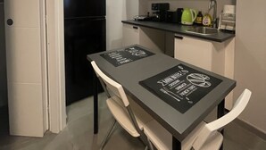 A compact kitchen with white cabinets, a black refrigerator, and a dining table with a placemat. - Pretty Studio Flat Moglio Alassio (Moglio)