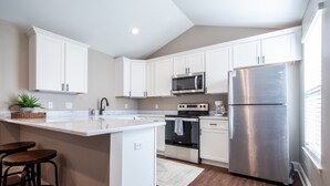 A modern kitchen with white cabinetry, stainless steel appliances, and a central island with stools. - The Bee, Cozy 1BR Studio by Velvet Ditch Villas (Oxford)