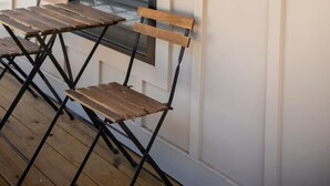 A wooden deck with two metal-framed tables and chairs, a window with blinds, and a black wall-mounted light fixture. - The Bee, Cozy 1BR Studio by Velvet Ditch Villas (Oxford)