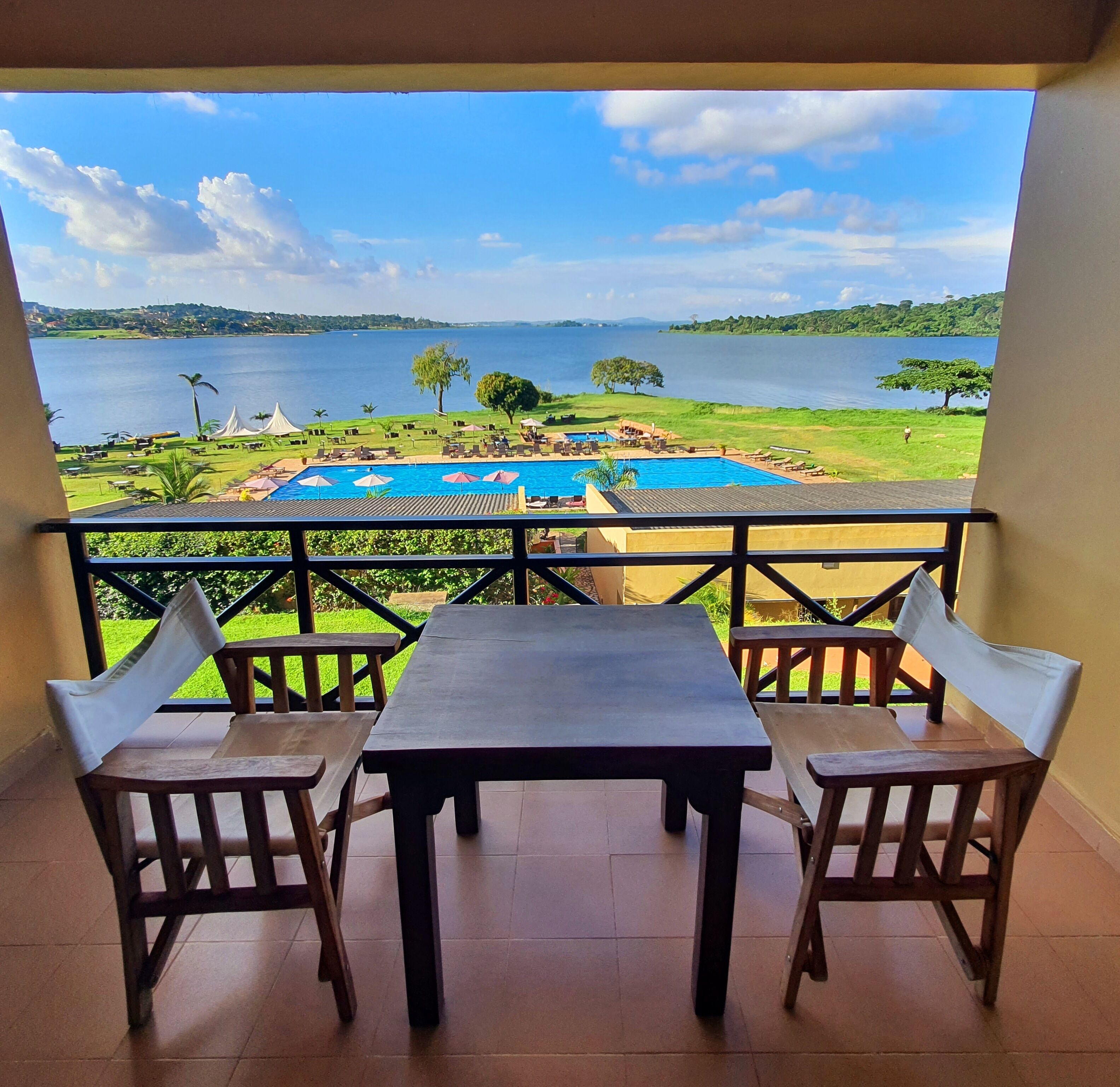 Un balcone con vista su un lago, una piscina e una zona verde con alberi.