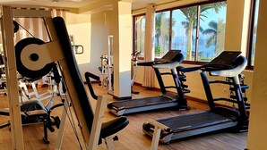 Ein Fitnessstudio mit Cardiogeräten, Krafttrainingsgeräten und einem großen Fenster mit Blick auf Palmen.