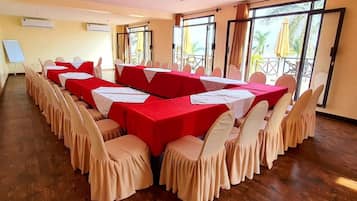 A conference room with multiple tables and chairs, large windows with curtains, and a whiteboard.