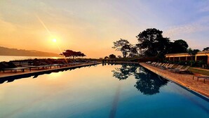 Ein Pool mit Liegestühlen und Blick auf den Sonnenuntergang über dem Wasser.