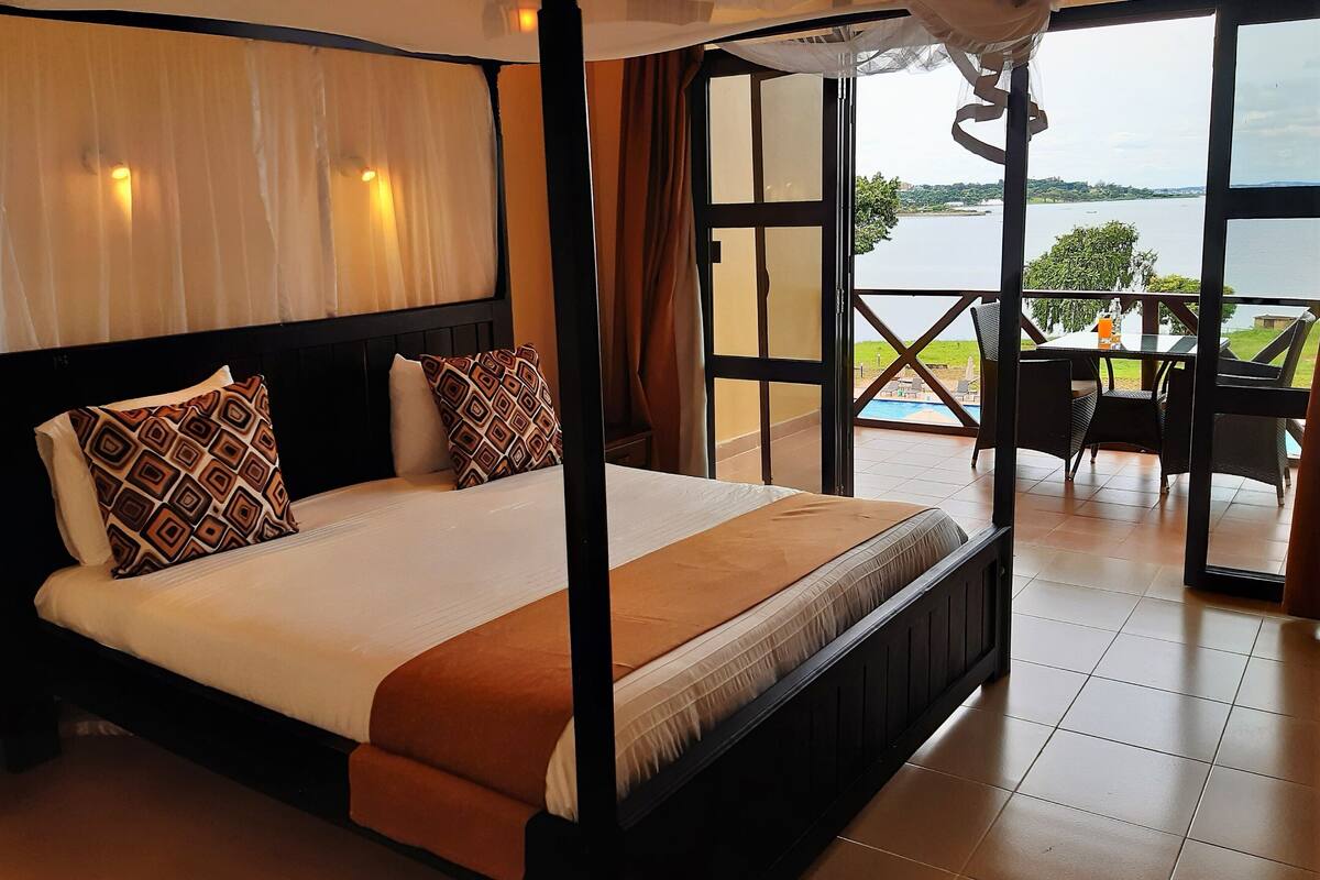 A hotel room with a large bed, a balcony with a view of the water, and a table with chairs.