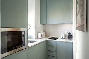 Cocina compacta con microondas integrado, hervidor, tostadora y un lavamanos pequeño.