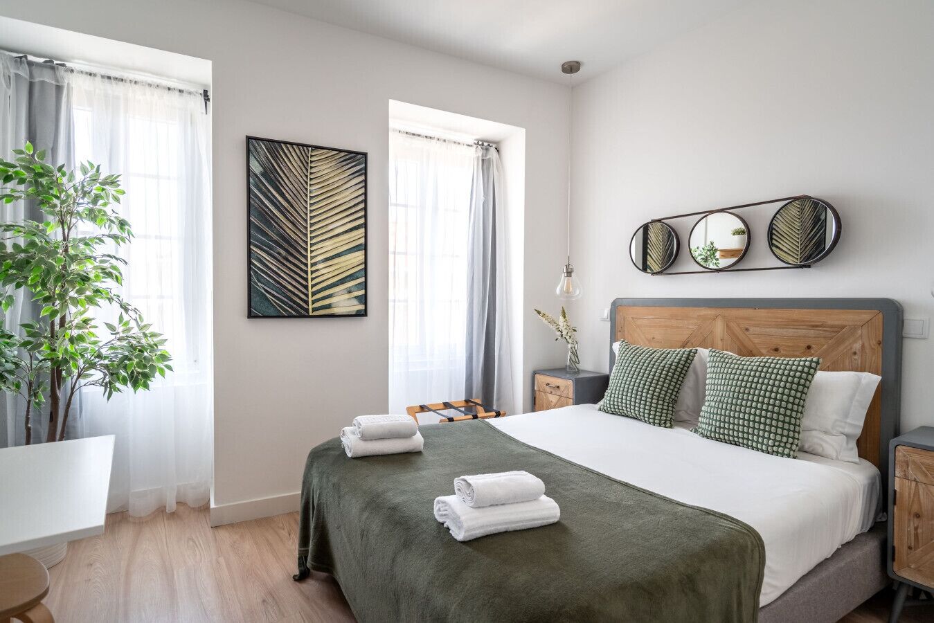 A neatly arranged bedroom with a bed, bedside tables, a mirror, and a potted plant.