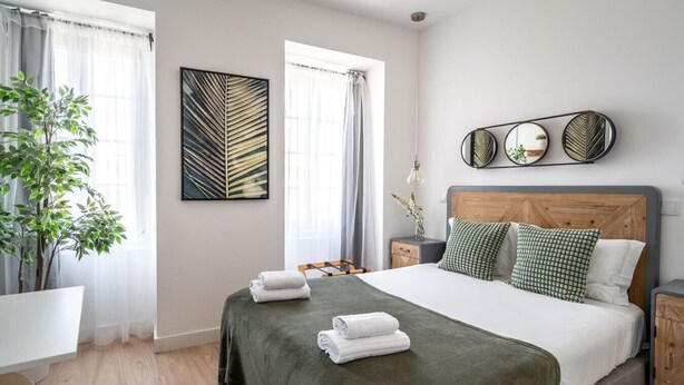 A neatly arranged bedroom with a bed, bedside tables, a mirror, and a potted plant. - Studio in Central Lisbon by Lisbeyond (Lisboa)