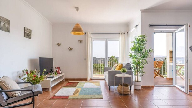 A modern living room with a sofa, a TV, a coffee table, and a balcony with outdoor furniture. - Beach & Nature Apartmentn in Aljezur by Lisbeyond (Aljezur)