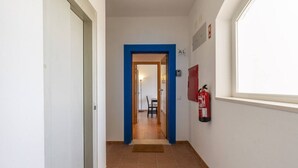 A hallway with a blue door frame, a fire extinguisher on the wall, and a window on the right. - Beach & Nature Apartmentn in Aljezur by Lisbeyond (Aljezur)