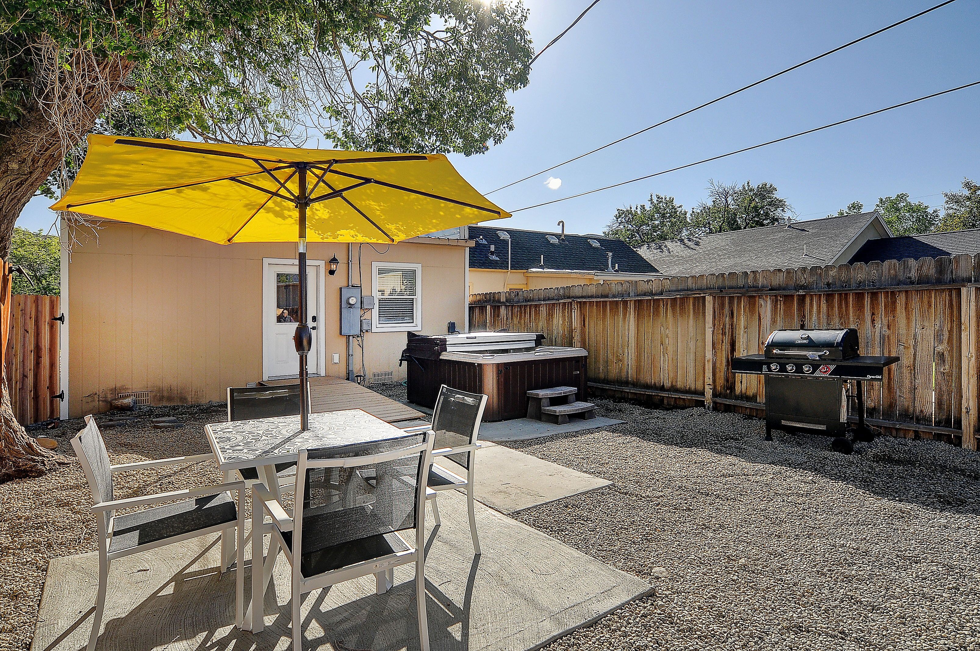 Un jardin avec une table de patio, des chaises, un parasol jaune, un jacuzzi et un barbecue.