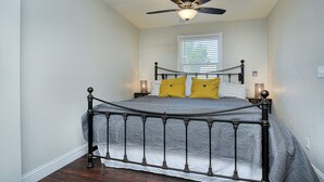 Ein Schlafzimmer mit einem Bett, Deckenventilator, Fenster mit Jalousien und Nachttischlampen.