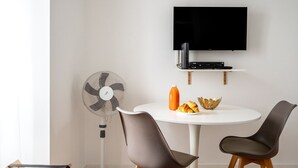 A modern dining area with a round table, two chairs, a wall-mounted TV, and a standing fan. - Studio with Stunning Views to river and old town by Lisbeyond (Lisboa)
