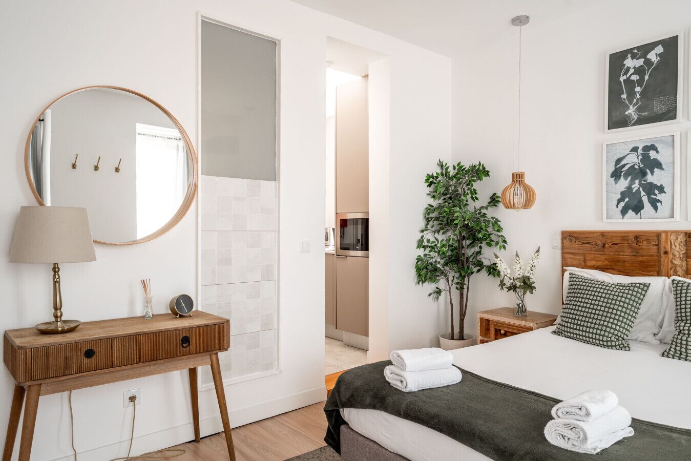 Un dormitorio con cama, mesitas de noche, un espejo, una planta en maceta y cuadros en la pared.