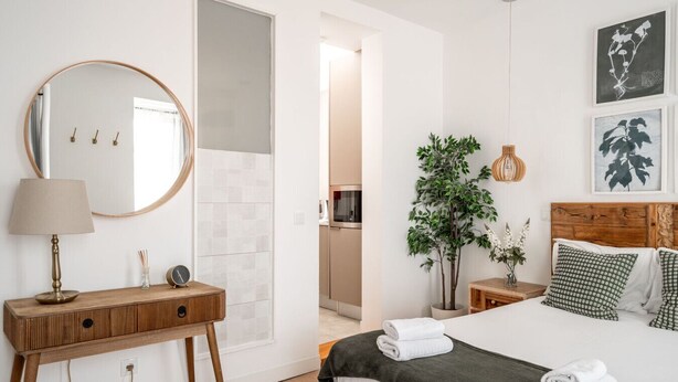 A bedroom with a bed, bedside tables, a mirror, a potted plant, and artwork on the wall. - Studio with Stunning Views to river and old town by Lisbeyond (Lisboa)
