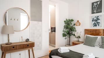 Un dormitorio con cama, mesitas de noche, un espejo, una planta en maceta y cuadros en la pared.