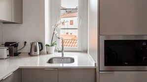 A modern kitchen with a stainless steel sink, a kettle, a toaster, and a view of a red-tiled roof through a window. - Studio with Stunning Views to river and old town by Lisbeyond (Lisboa)