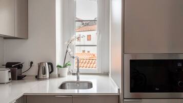 Una cocina moderna con un lavabo de acero inoxidable, una tetera, un tostador y vistas a un tejado de tejas rojas a través de una ventana.