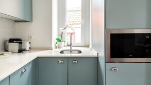 Une cuisine moderne avec des armoires de couleur turquoise, un évier en acier inoxydable, un grille-pain et une fenêtre donnant sur un immeuble.
