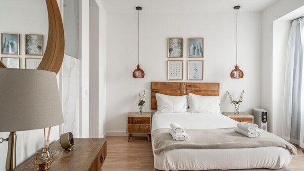 Une chambre moderne avec une tête de lit en bois, une table de chevet avec une lampe, une commode et un lit sur lequel sont soigneusement pliées des serviettes.