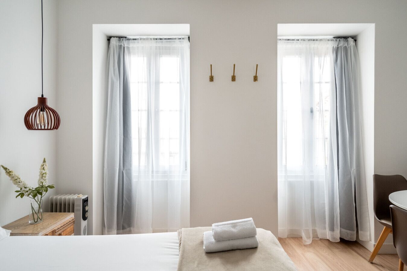 Une chambre à coucher avec un lit, une table de chevet ornée d’un vase, un radiateur et une chaise.