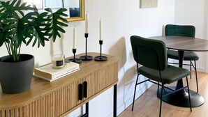 A modern dining area with a wooden console table, a green upholstered chair, and a round table. - Stay in the heart of Alfama! | Cozy Apartment (Lisboa)