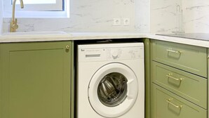 A compact kitchen with green cabinets, a built-in washing machine, and a window above the sink. - Stay in the heart of Alfama! | Cozy Apartment (Lisboa)