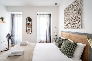 A modern bedroom with a large bed, two bedside tables, a wall-mounted mirror, and a decorative wall piece. - Lively Studio in Historic Center of Lisbon by Lisbeyond (Lisboa)