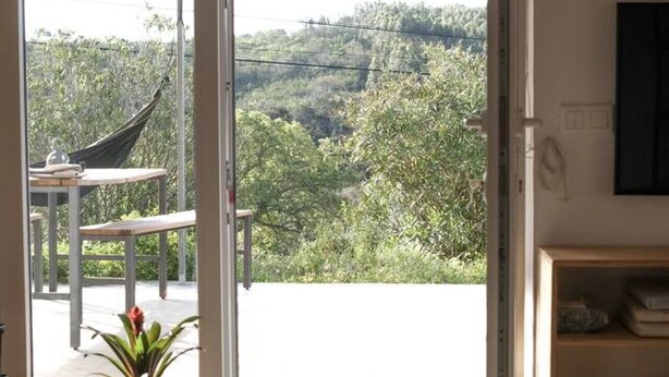 Une pièce dotée d’une grande porte-fenêtre coulissante donnant sur un espace extérieur aménagé avec un hamac et une table. On y trouve également une plante en pot.