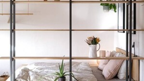 Une chambre de style loft moderne avec un plafond en bois, une suspension noire, un lit avec une tête de lit blanche et un banc intégré agrémenté d’une plante.