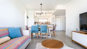A modern living room with a sofa, dining table, chairs, and a TV. - Oasis Mar Beach Apartment by Lisbeyond (Portimão)
