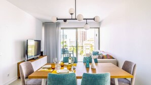 A modern dining area with a wooden table, teal chairs, and a television on a cabinet. - Oasis Mar Beach Apartment by Lisbeyond (Portimão)