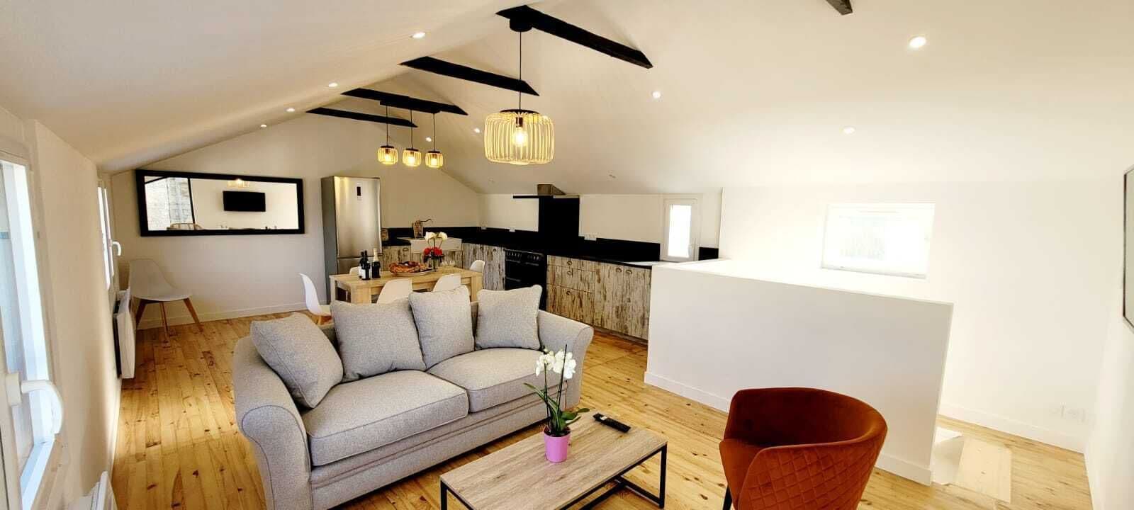 Un salon moderne avec un canapé gris, une table basse en bois et un fauteuil rouge. On y trouve également un coin cuisine avec un comptoir noir et un luminaire suspendu.