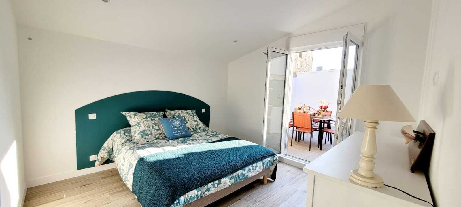 A bedroom with a bed, a bedside lamp, and a view of an outdoor dining area through a sliding door.