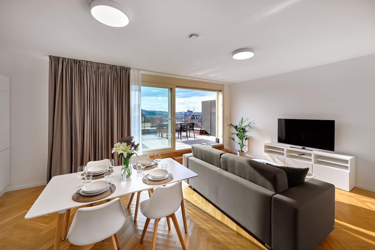 A modern living room with a dining area, large windows, and a flat-screen TV.