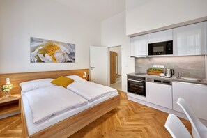 Een moderne hotelkamer met een houten bed, een keuken met witte kasten en een groot bloemen schilderij aan de muur.