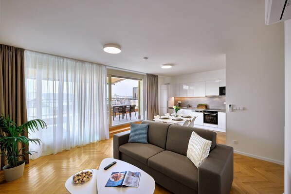 Een moderne woonkamer met een bank, salontafel en een zichtbare eethoek door een groot raam.