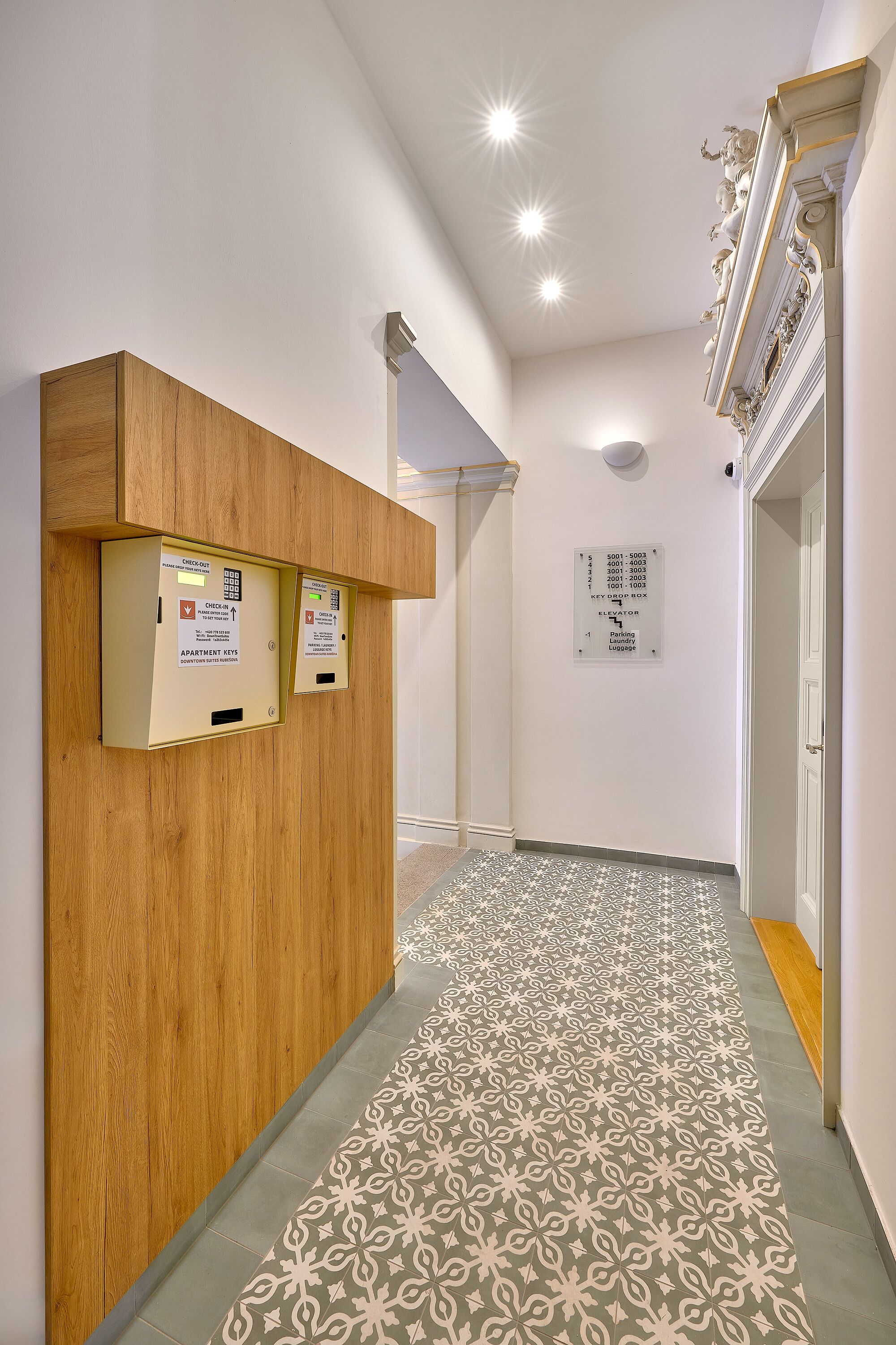 A hallway with a patterned floor, wooden reception desk, and a wall-mounted elevator control panel.