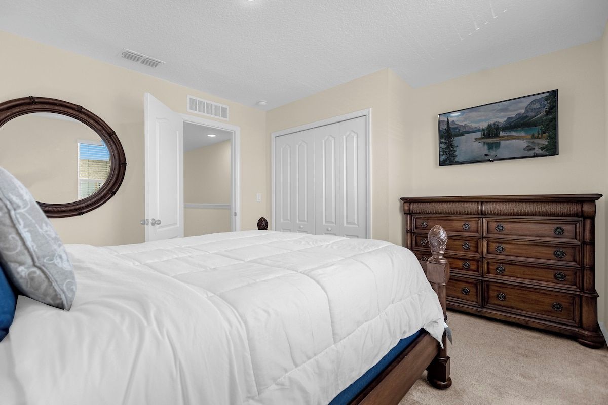 A bedroom with a bed, a dresser, a mirror, and a painting on the wall.