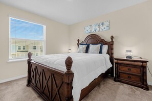 A bedroom with a wooden bed, a nightstand, a window with blinds, and a wall with three framed pictures. - 4730 Lakeview Townhome with Pool Access Near Disney (Kissimmee)