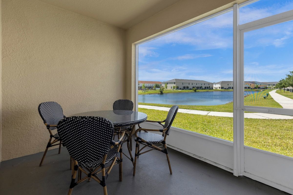 A balcony with a table and chairs, overlooking a body of water and buildings.