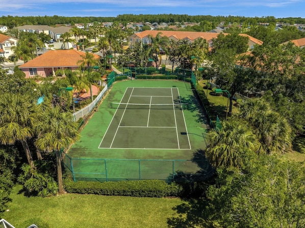 A tennis court surrounded by greenery and residential buildings.