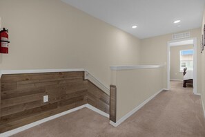 A hallway with a wooden accent wall, a fire extinguisher mounted on the wall, and a carpeted floor. - 4730 Lakeview Townhome with Pool Access Near Disney (Kissimmee)