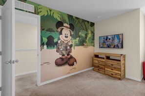 Una habitación con un mural de Mickey Mouse en la pared, un aparador de madera y un cuadro enmarcado.