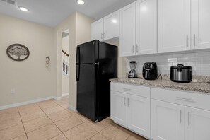 Una cocina con armarios blancos, un refrigerador negro, una cafetera y una licuadora.