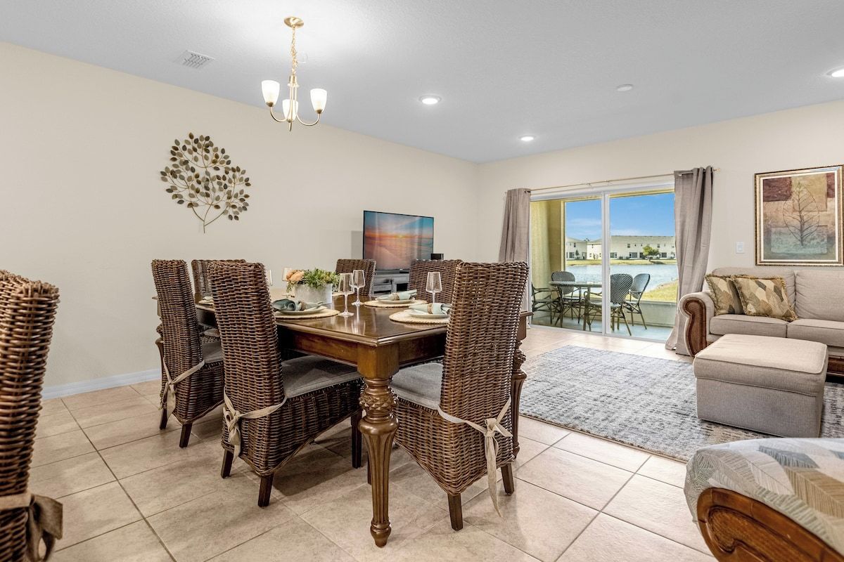 A dining area with wicker chairs, a wooden table, and a chandelier.