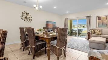 A dining area with wicker chairs, a wooden table, and a chandelier.