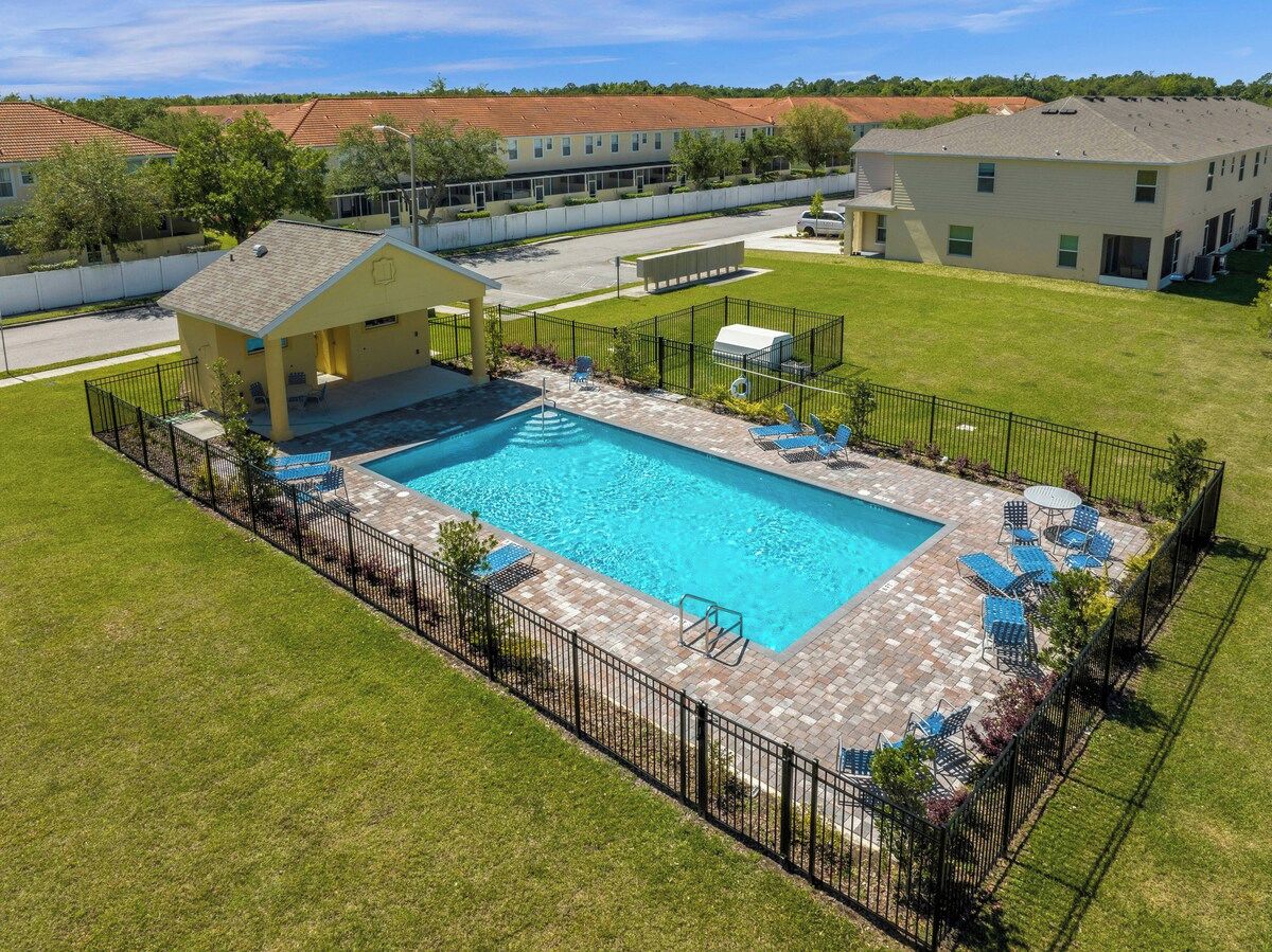 A rectangular swimming pool with a paved deck, surrounded by a black metal fence.
